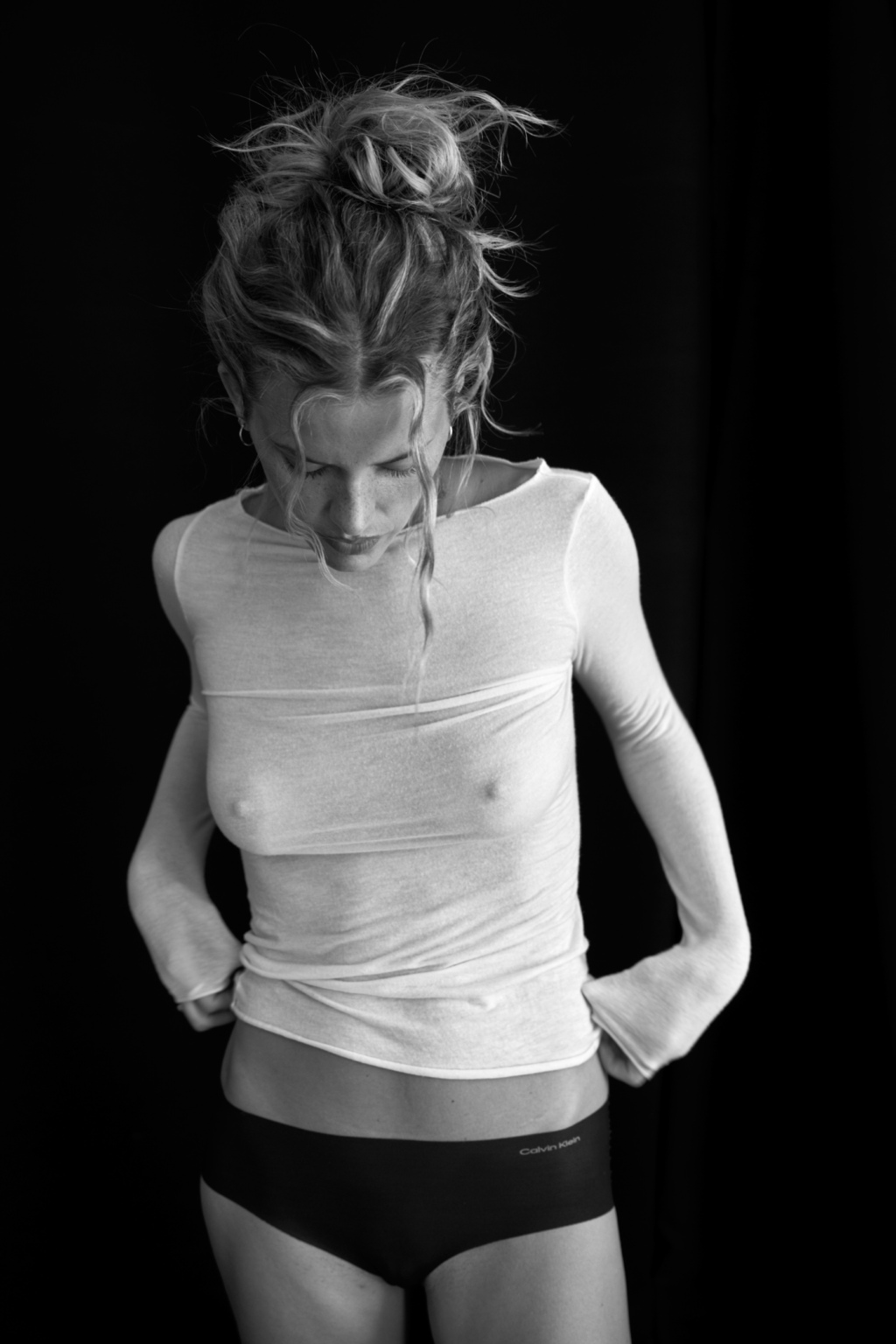 Black and white image of a young woman wearing a long sleeve tight shirt and black underwear