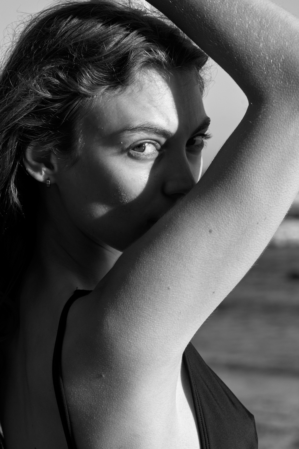 Black and white portrait of young woman at the beach looking through her bent raised arm
