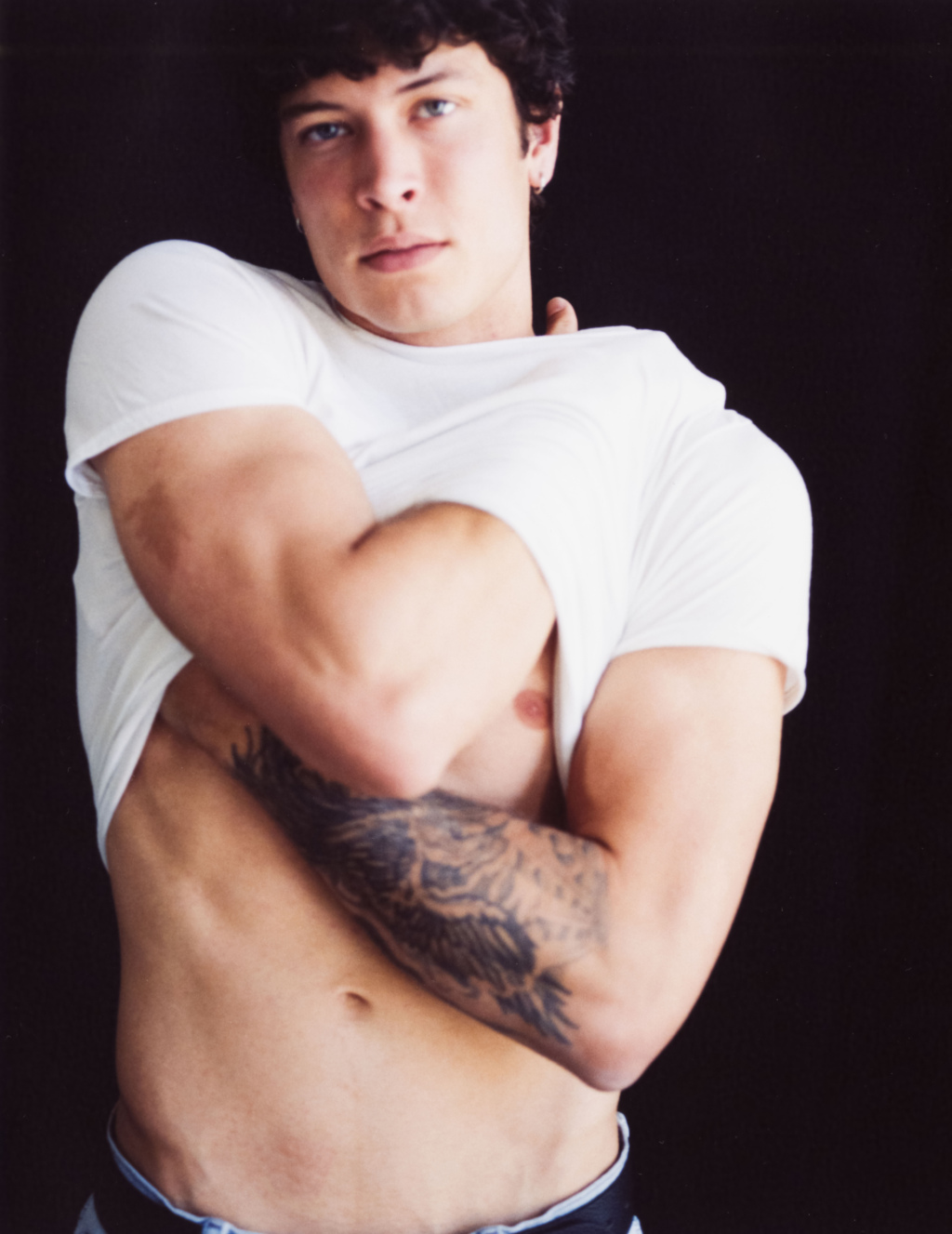 Young man hugging himself in a white t-shirt that shows his torso