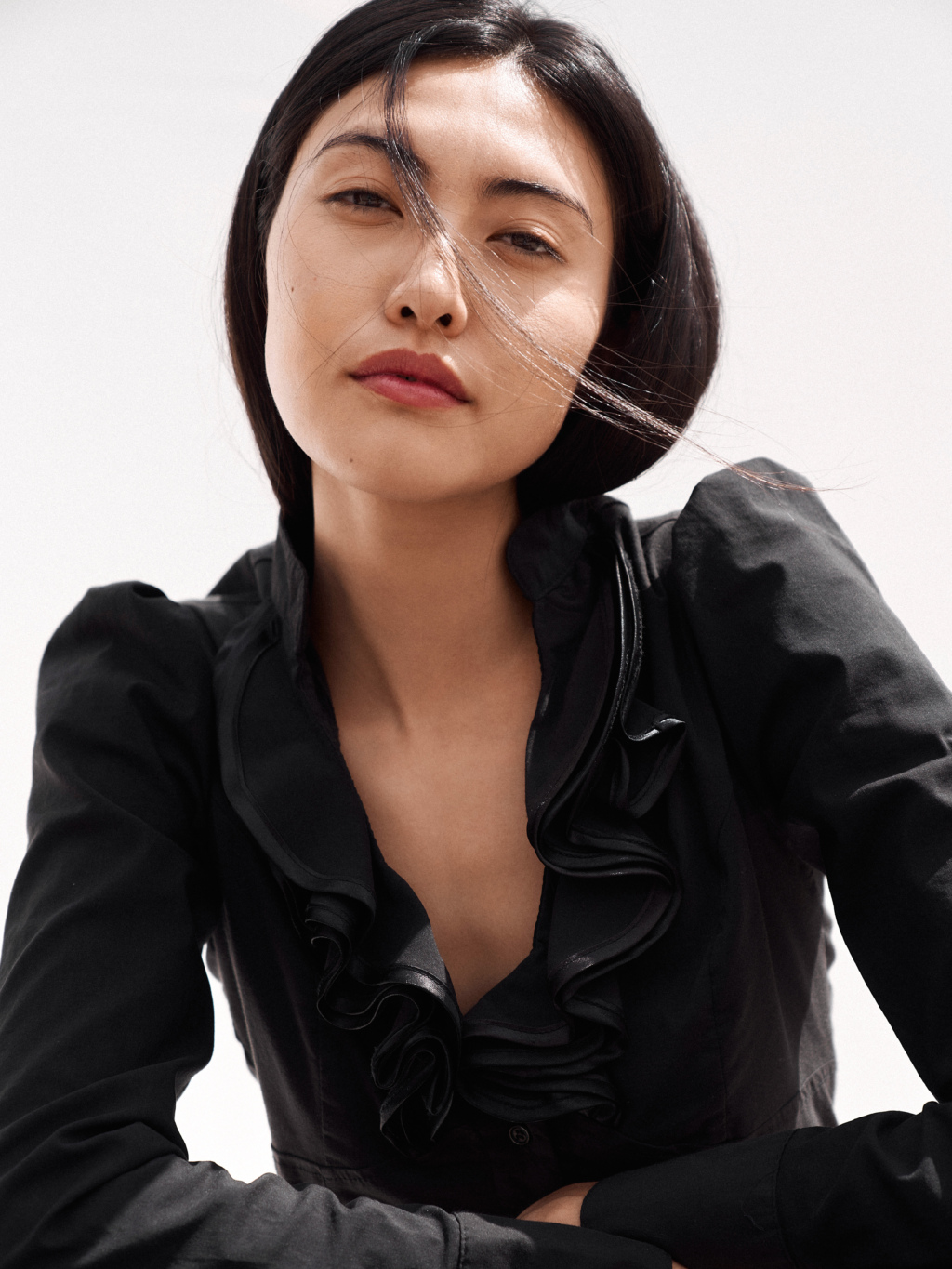Portrait of a woman wearing a black blouse with exaggerated shoulders, a strand of hair over her eyes