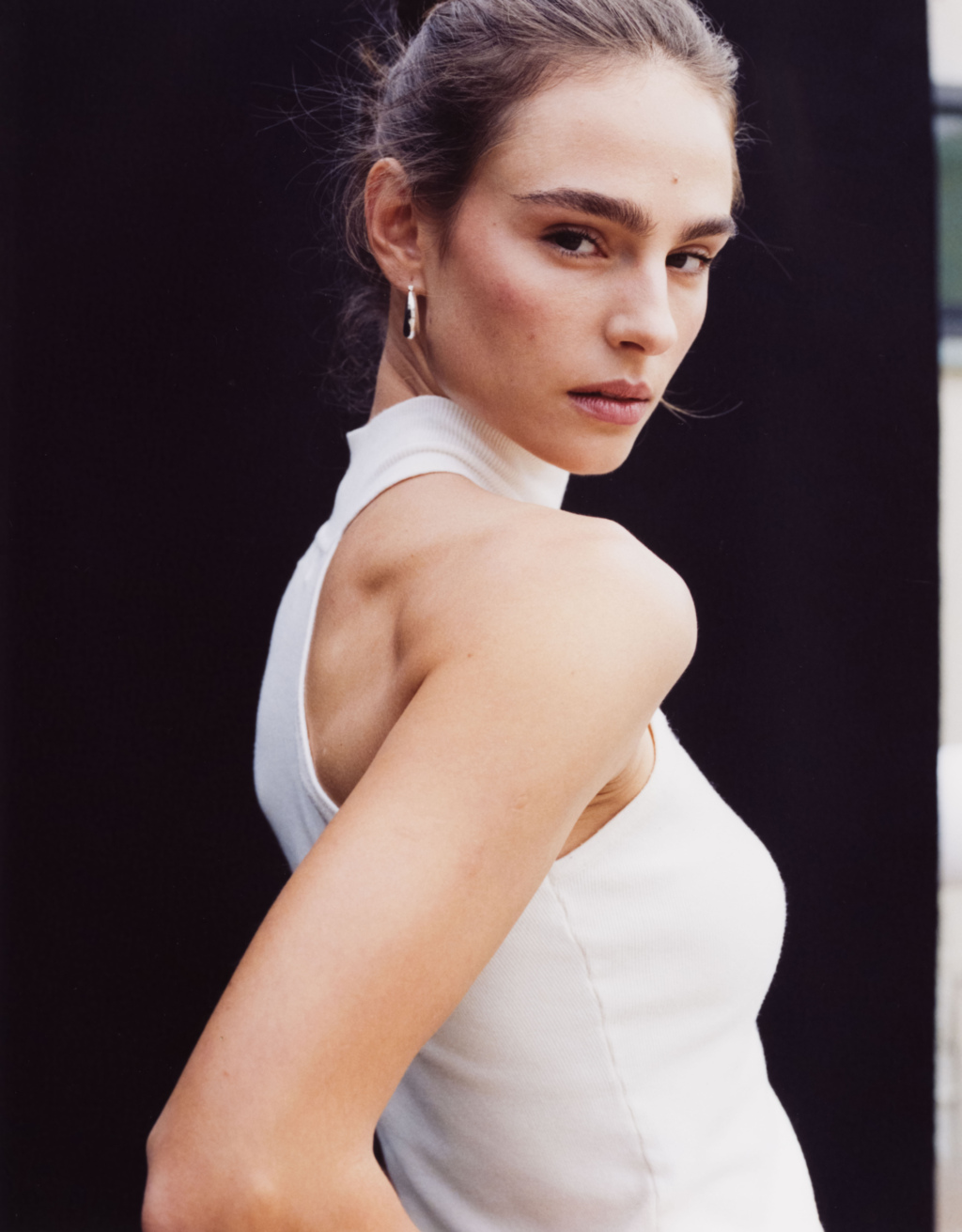 Portrait of a young woman wearing a white top against a black background