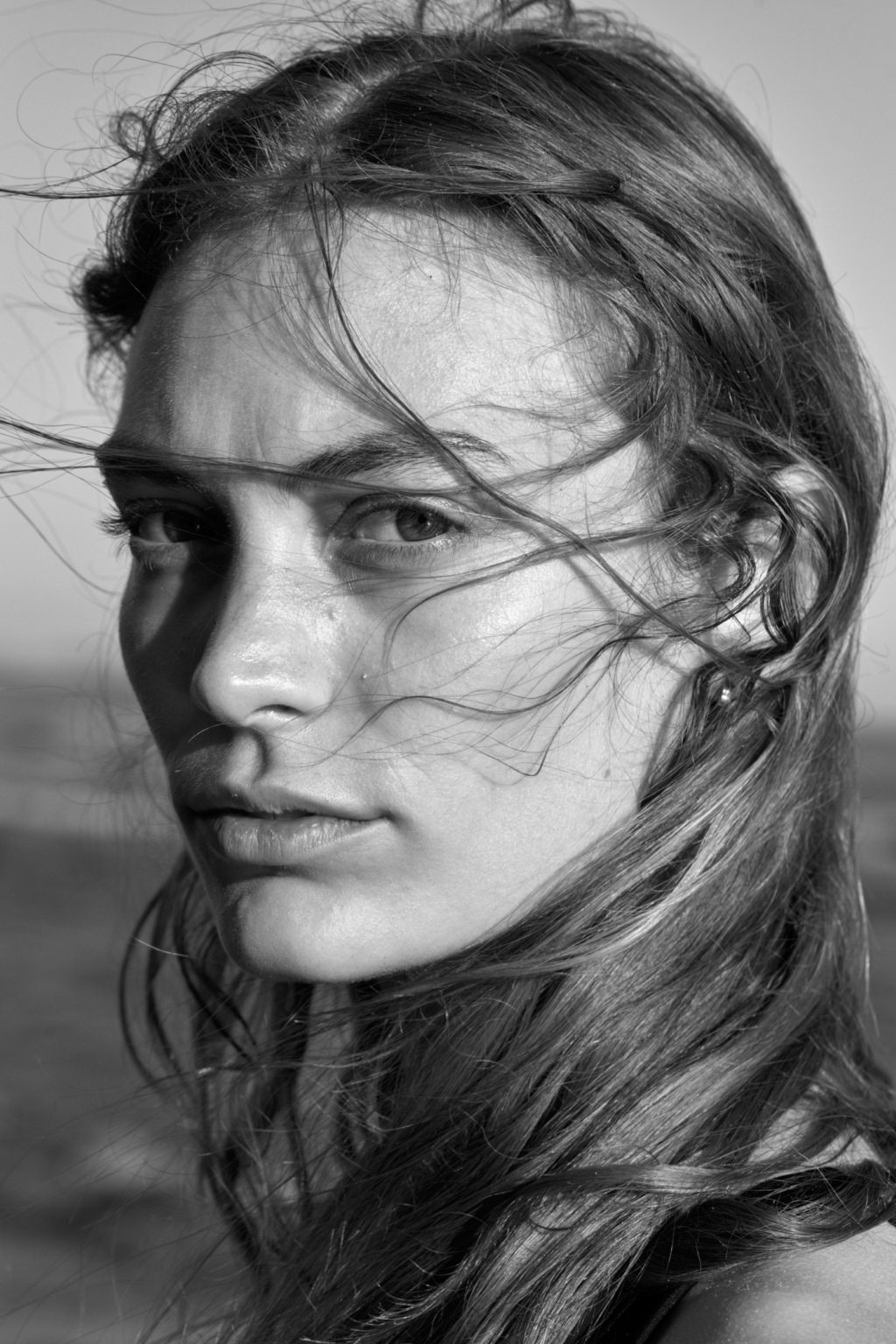 Black and white portrait of young woman at the beach, hair blown by wind