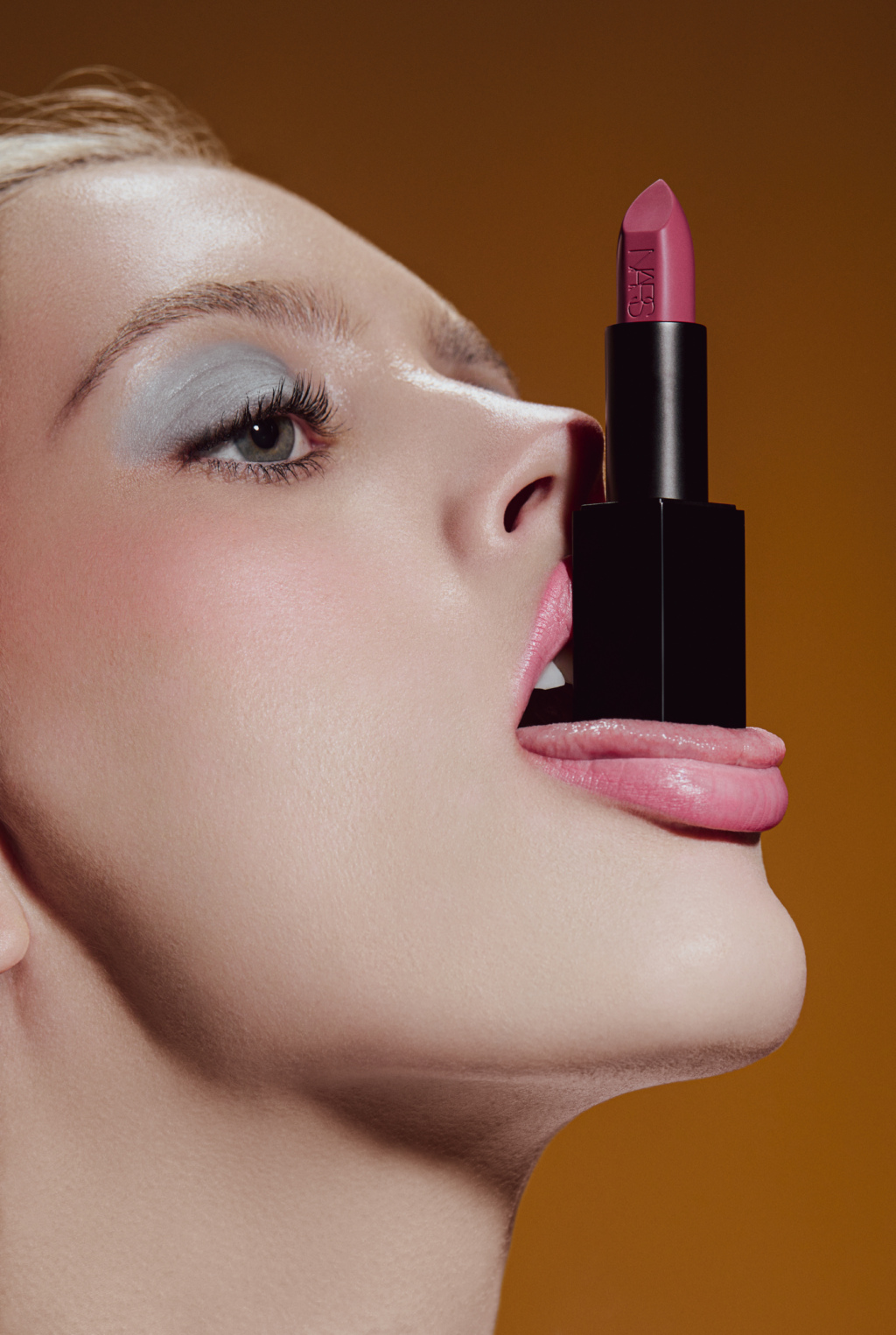 Tight shot of a woman's face with a lipstick resting on her tongue