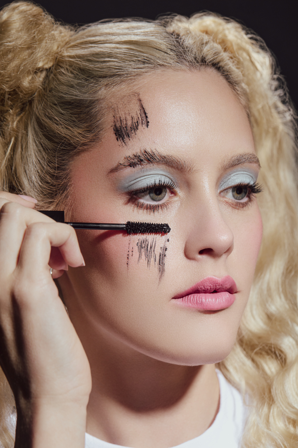 Young blonde woman puts mascara on her cheek